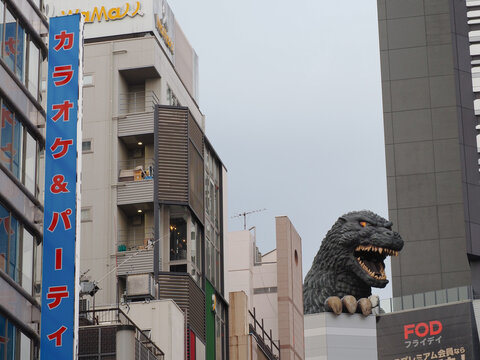 TOKYO, JAPAN - January 7, 2025: View of Shinjuku with sign on a Karaoke Kan karaoke center and statue of Godzilla on a Toho movie theatre. There's a poster advertising Fuji FOD streaming service.
