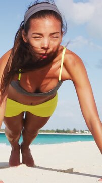 Determined young fitness woman exercising pushups on sea shore. Sporty female doing muscular training against sky. Girl on beach in summer. Video is unretouched and model without makeup. Raw footage.