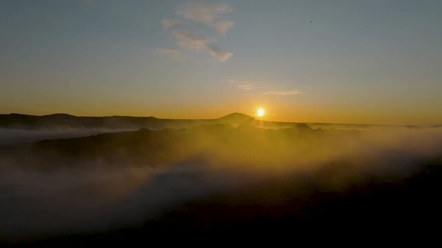 Aerial view of a golden sunset over a misty volcanic landscape with rolling hills and low clouds in Grimsey, Reykjanesbaer, Iceland.