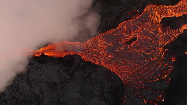 Aerial view of glowing lava flowing over dark volcanic rock with thick steam rising in Reykjanesbaer, Iceland.