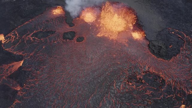 Aerial view of glowing molten lava erupting from a volcanic fissure, flowing across dark solidified basalt rock in Reykjanesbaer, Iceland.