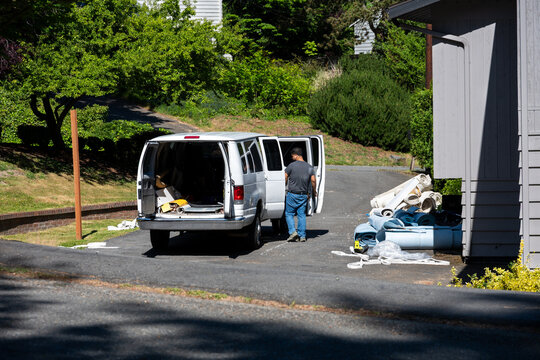 Workman at van, remodeling and updating residential house, new carpet installation in progress, piles of under carpet padding and rug
