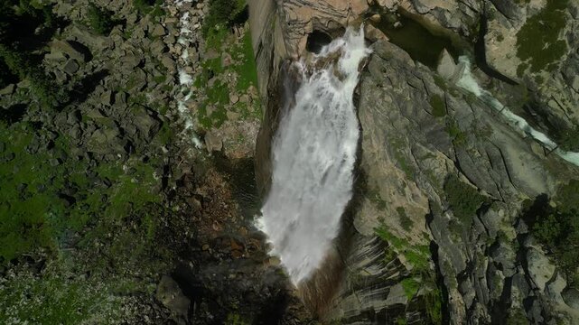 Aerial shot of Yosemite Valley featuring cascading waterfall surrounded by granite cliffs, dense forest, and dramatic mountain landscape in California&rsquo;s Sierra Nevada.