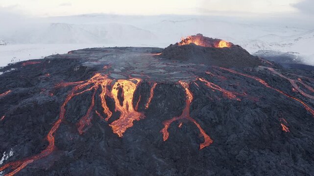 Aerial view of glowing lava flowing from a volcanic crater across dark solidified rock fields in Reykjanesbaer, Iceland.