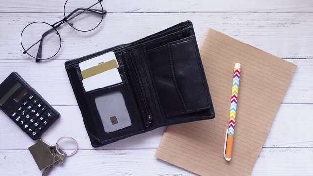 Top view of open wallet with credit cards, notebook, pen, glasses, calculator and keys on wooden table