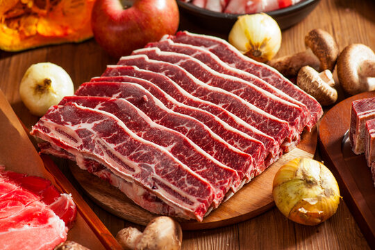 Raw Beef Short Ribs: Fresh Marbled LA Galbi Slices Arranged on Wooden Cutting Board with Cooking Ingredients