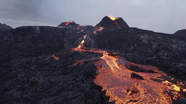Aerial view of glowing lava flowing from a volcanic eruption across the dark basalt landscape of the Reykjanes Peninsula in Reykjanesbaer, Iceland.