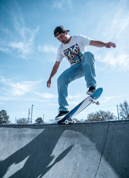 Low angle shot of a young active man performing a skateboard trick midair on a concrete ramp at an outdoor skatepark against a blue sky.