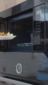 Woman takes plate with meal from built in microwave oven. Concept of food reheating and home cooking.