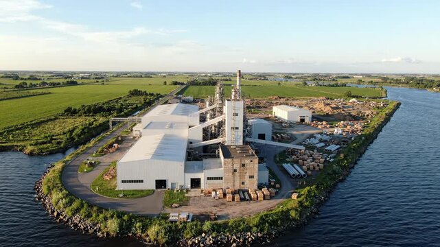 Aerial view of a large industrial facility situated on a small island surrounded by water and green fields under a blue sky