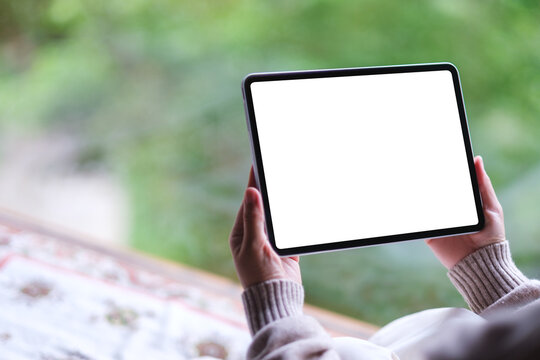 Mockup image of a woman holding tablet with blank desktop white screen on the bed at home