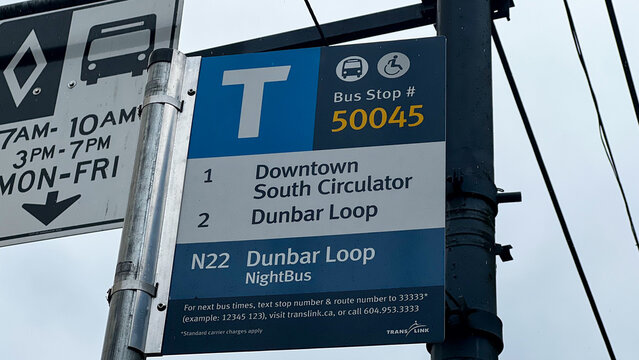 Close-up of a TransLink bus stop number 50045 sign, its blue T logo above routes to Downtown, South Circulator and Dunbar Loop plus the N22 NightBus, on a metal pole.