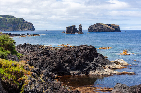 Ilheus dos Mosteiros with its iconic rock formations in the ocean. The rocky coastline of Sao Miguel island in the Azores. Clear blue waters and sky meet volcanic cliffs.