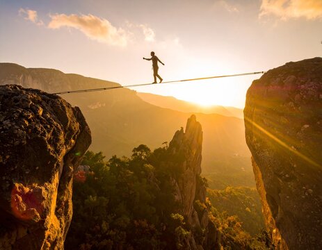 Adventurous person balancing on a highline between two rocky mountain peaks during a stunning golden sunset