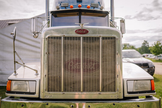 Peterbilt truck front view showcasing chrome grille and headlights, parked in an outdoor setting with cloudy sky in the background