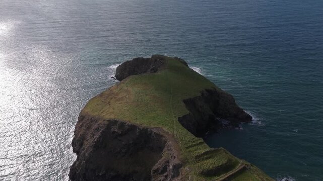 Aerial view of the rugged Welsh Coast headland with steep cliffs and grassy slopes overlooking the shimmering blue sea in St Davids, Wales, United Kingdom.