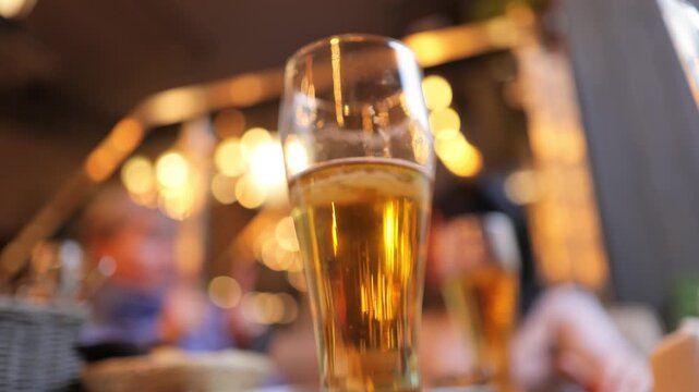 Close up of refreshing golden beer in glass with bokeh background and people chatting.