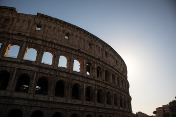 Naklejka premium Inquadratura dal basso delle storiche arcate del Colosseo a Roma illuminate dalla luce calda del sole, antico monumento romano simbolo dell'Italia e patrimonio dell'umanità UNESCO
