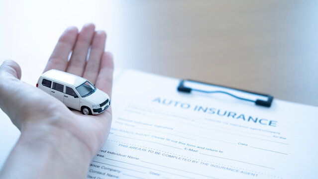 White toy car protected in a hand over an auto insurance contract, symbolizing vehicle insurance, safe driving, policy coverage and financial protection.