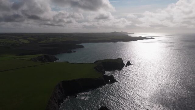 Aerial view of the rugged Welsh Coast featuring steep cliffs and green fields overlooking the sea under a cloudy sky St Davids, Wales, United Kingdom.