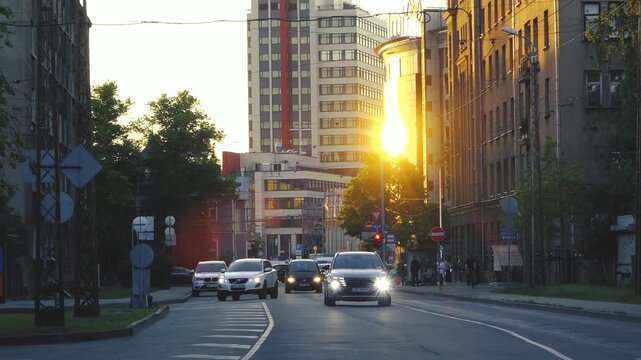City street at sunset with cars driving between tall buildings, warm sunlight reflecting on facades, traffic signs, and evening urban atmosphere. Riga, Latvia - June, 12, 2026.