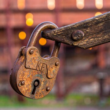Rusty padlock hanging from a wooden beam