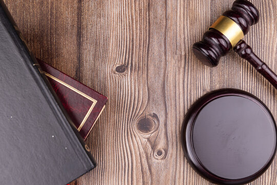 Cenital view of a person hand holding a mahogany judge gavel near antique criminal law books over a dark rustic wooden desk surface