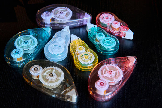 A collection of colorful transparent correction tape dispensers with visible internal gear mechanisms on a dark table surface.