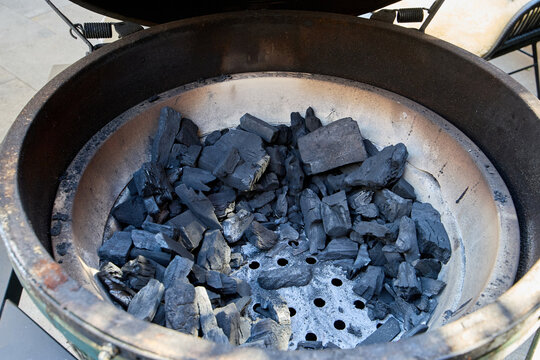 Black charcoal briquettes inside a kamado ceramic grill bowl before lighting, prepared for an outdoor barbecue cooking session.