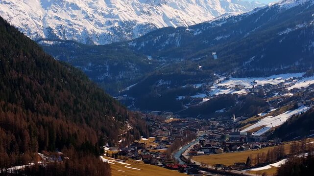 Aerial view of the town of Soelden nestled in a deep valley surrounded by snow-capped mountains and dense evergreen forests in Soelden, Tyrol, Austria.