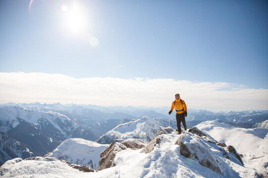 Male hiker in an orange jacket on a snowy mountain peak