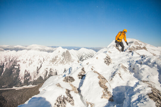 Man in orange jacket climbs snowy mountain ridge