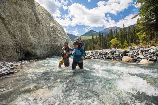 Friends helping woman cross a fast mountain river