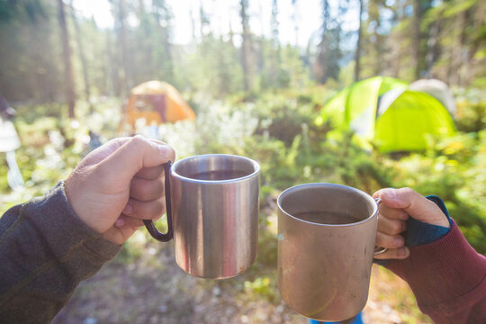 Couple toasting with metal mugs at campsite