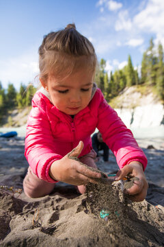 Curious little girl sifting sand through her hands