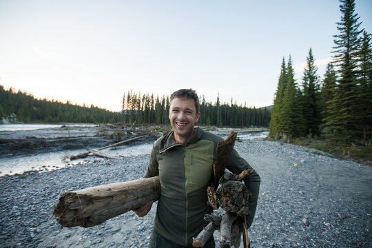 Happy man carries firewood for a campfire by the river
