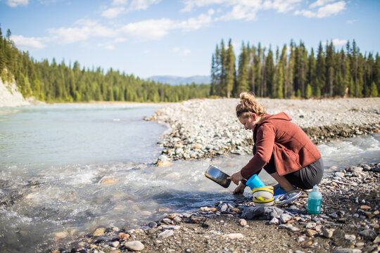 Woman washing camping dishes in a mountain river