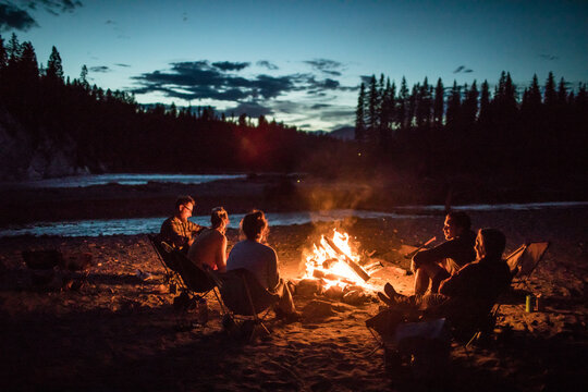 Group of friends enjoy a bonfire by the river at dusk