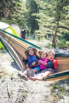 Three kids smiling and laughing in a camping hammock