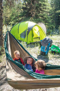 Happy children smile from a hammock while camping