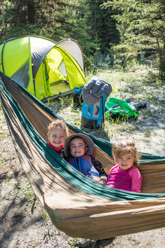 Three kids smiling together in a camping hammock