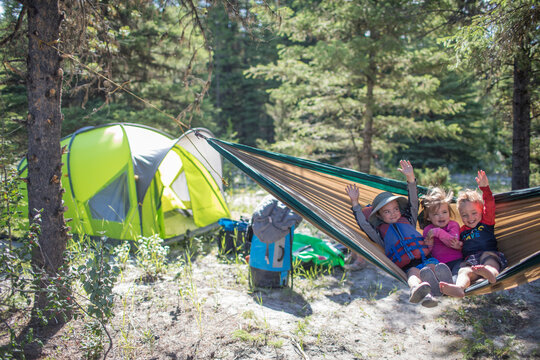 Happy children waving from a hammock at campsite
