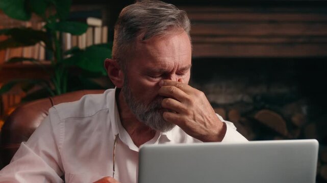 Stressed overworked Caucasian old senior business man talking off glasses rubbing face tired with laptop work online difficult job aged retired businessman rub eyes feeling migraine headache at office