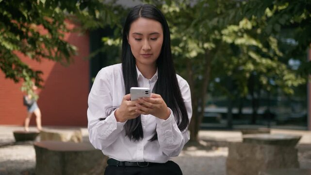 Asian Korean business woman thinking coming up with idea chatting with mobile phone in city Japanese Chinese businesswoman female girl finding decision female think scrolling website cellphone service