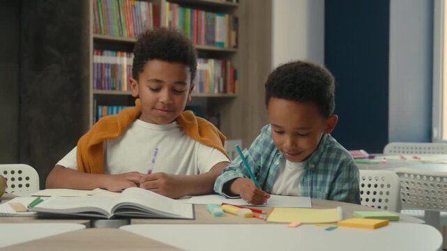 Two cute kids African American boys together learning writing in kindergarten smiling enjoy elementary primary education children sons pupils study learn write smile joyful studying process in library