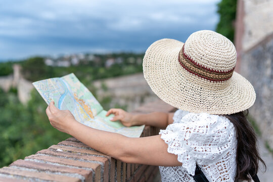 Latin woman wearing straw hat navigating city with map enjoying vacation in Girona, Spain