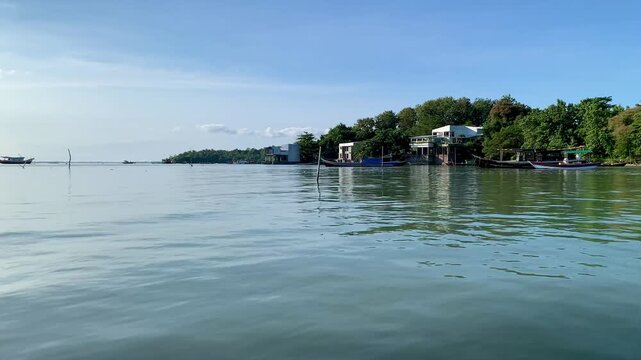 4K serene view of Tanjung Lesung Beach, Banten, Indonesia, with gentle rippling waves, calm shoreline, boats and coastal greenery under a vast blue sky. Ideal for travel, nature, summer and relaxation