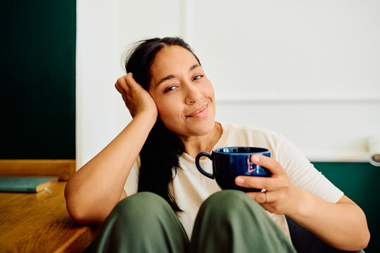 Woman smiling, relaxing at home, holding a cup of coffee. Embracing comfort and a peaceful morning moment