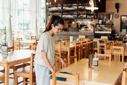 A working student with a part-time job cleans a restaurant table while preparing for customers before opening hours.