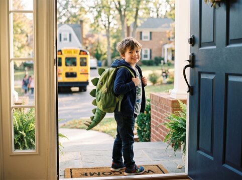 Ready for Adventure: A young boy, equipped with a fun dinosaur backpack, stands at his front door, ready for a new day of learning and fun as a school bus waits nearby.